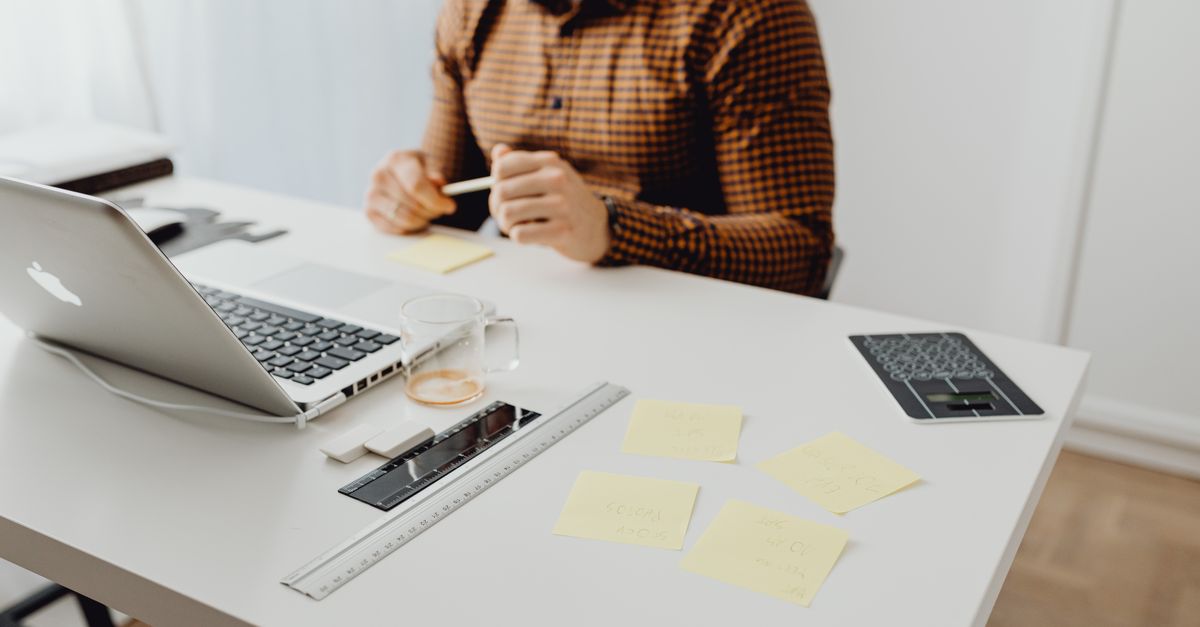 Modern workspace setup with laptop, office supplies, and a person in a checked shirt.